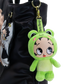 A green plush keychain shaped like a cartoon frog character with large eyes and a Betty Boop strap, hanging from a black bag against a white background.