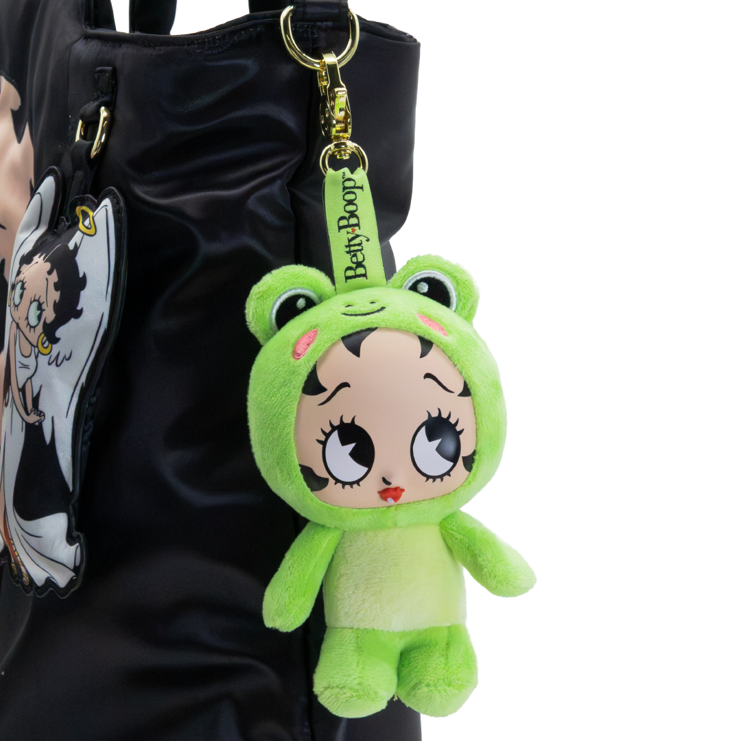 A green plush keychain shaped like a cartoon frog character with large eyes and a Betty Boop strap, hanging from a black bag against a white background.