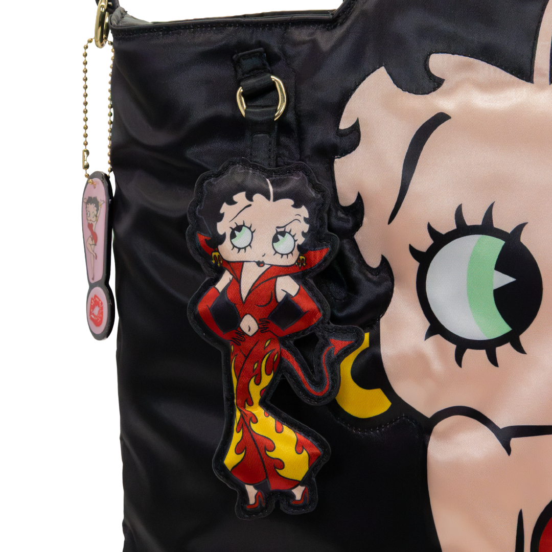 Close-up of a black satin handbag featuring a large Betty Boop face graphic and a hanging Betty Boop character charm in a red and yellow dress.