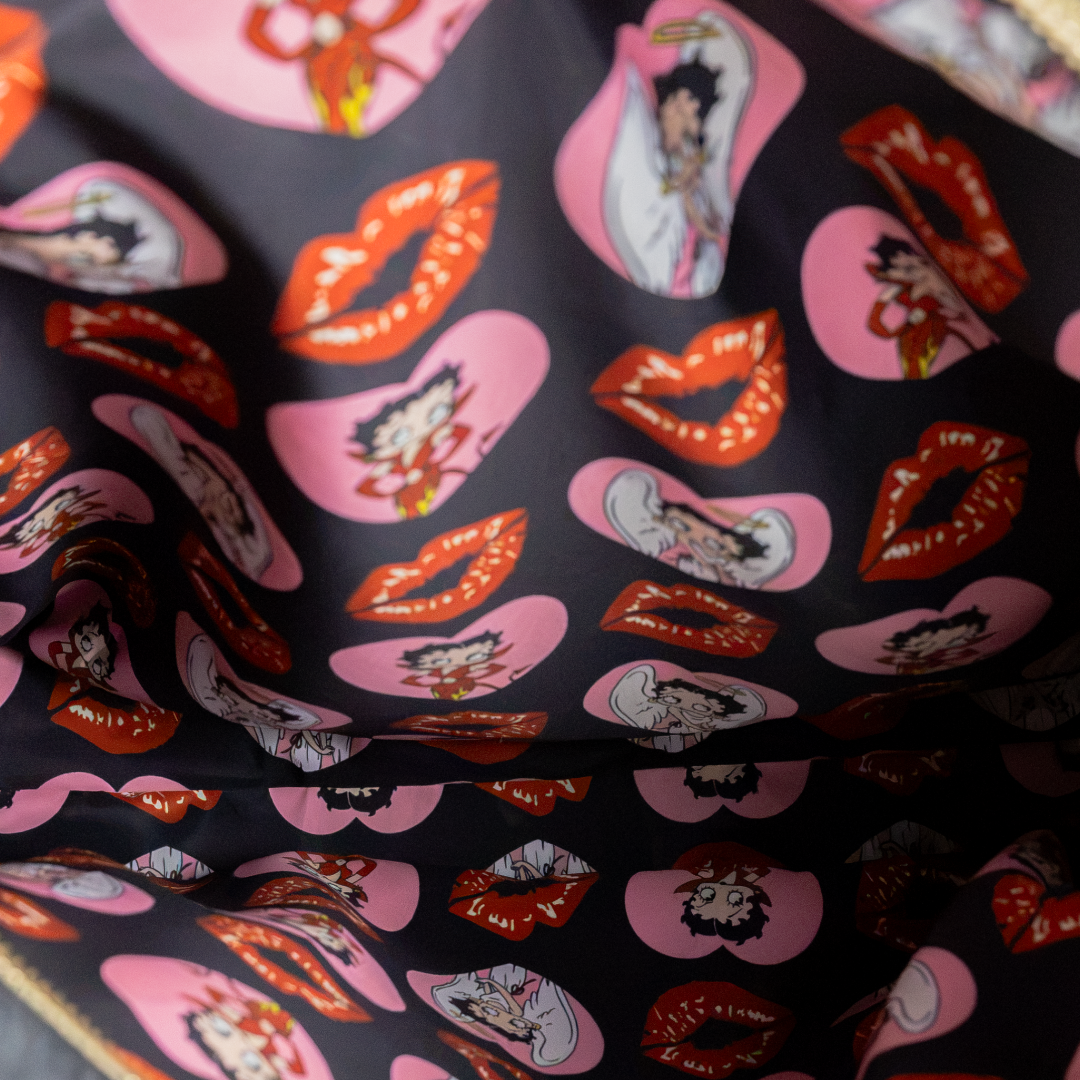 A close-up of a black fabric printed with pink hearts, red lips, and Betty Boop character illustrations.