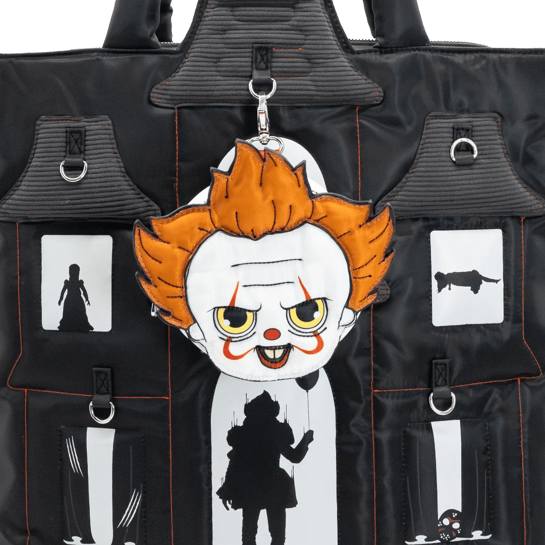 A black nylon tote bag with multiple utility pockets, featuring a hanging plush keychain of a creepy clown character with orange hair, white face, and red and yellow details.