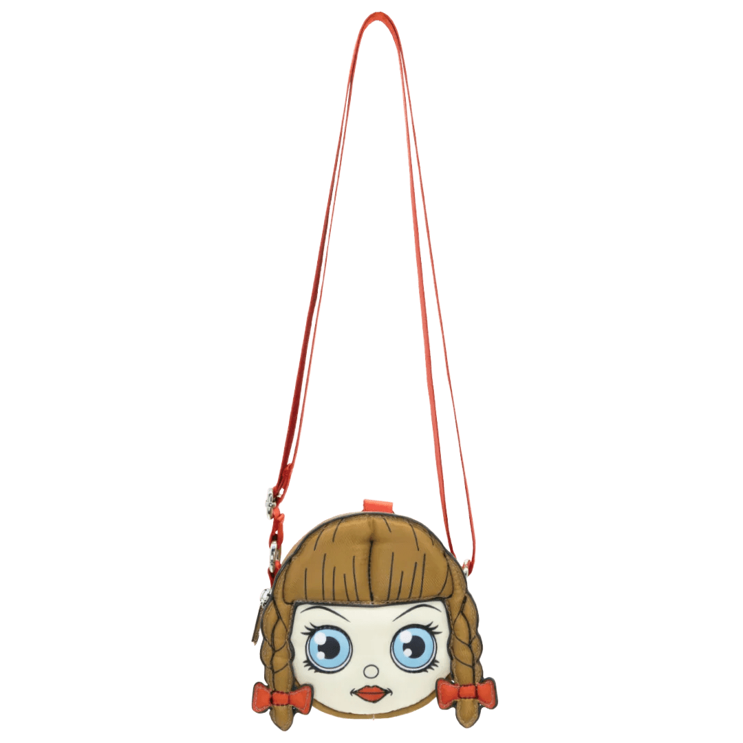 A small shoulder bag shaped like a cartoon girl's face, featuring brown hair in braids, large blue eyes, and red accents, with a long red strap on a plain white background.