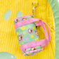 Small green pouch with pink strap and floral patterns on a yellow textured background