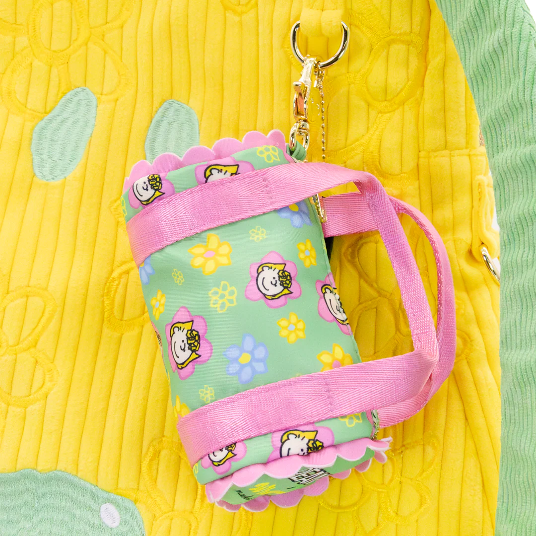 Small green pouch with pink strap and floral patterns on a yellow textured background