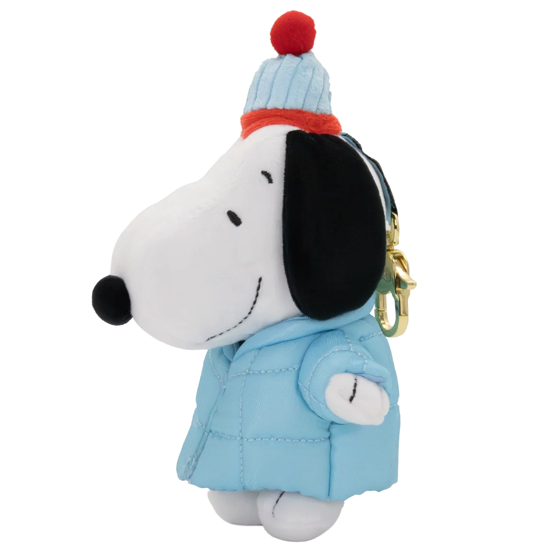 A plush keychain of Snoopy wearing a light blue quilted winter coat and a light blue knit beanie with a red pom-pom and orange band, attached to a gold keyring, on a white background.