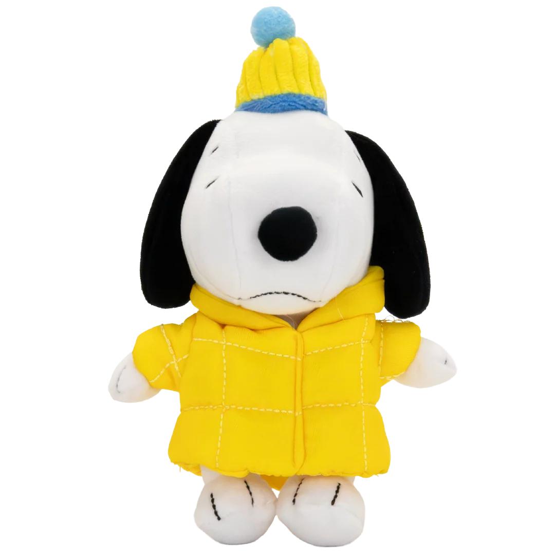 A plush toy of Snoopy wearing a yellow quilted jacket and a yellow and blue knit beanie hat, set against a plain white background.
