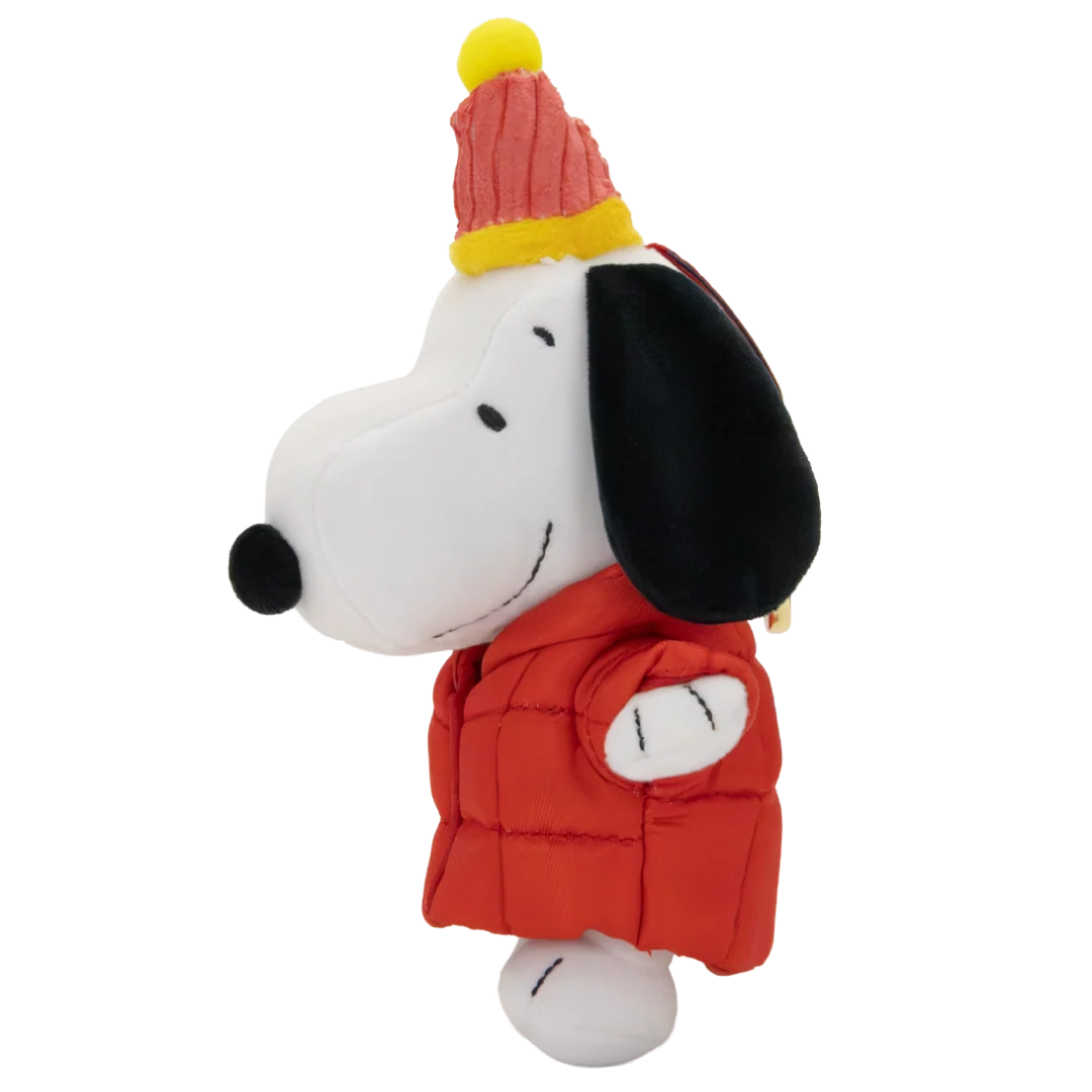 A plush toy of Snoopy wearing a red puffer jacket and a red and yellow knit party hat, set against a plain white background.