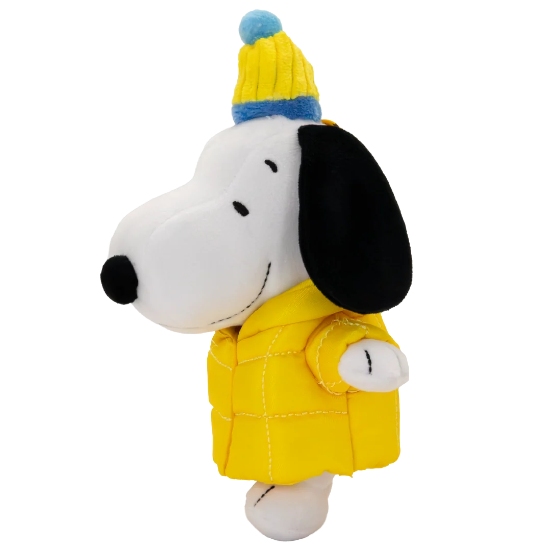 A plush toy of Snoopy wearing a yellow puffer jacket and a yellow and blue knit beanie hat, set against a plain white background.