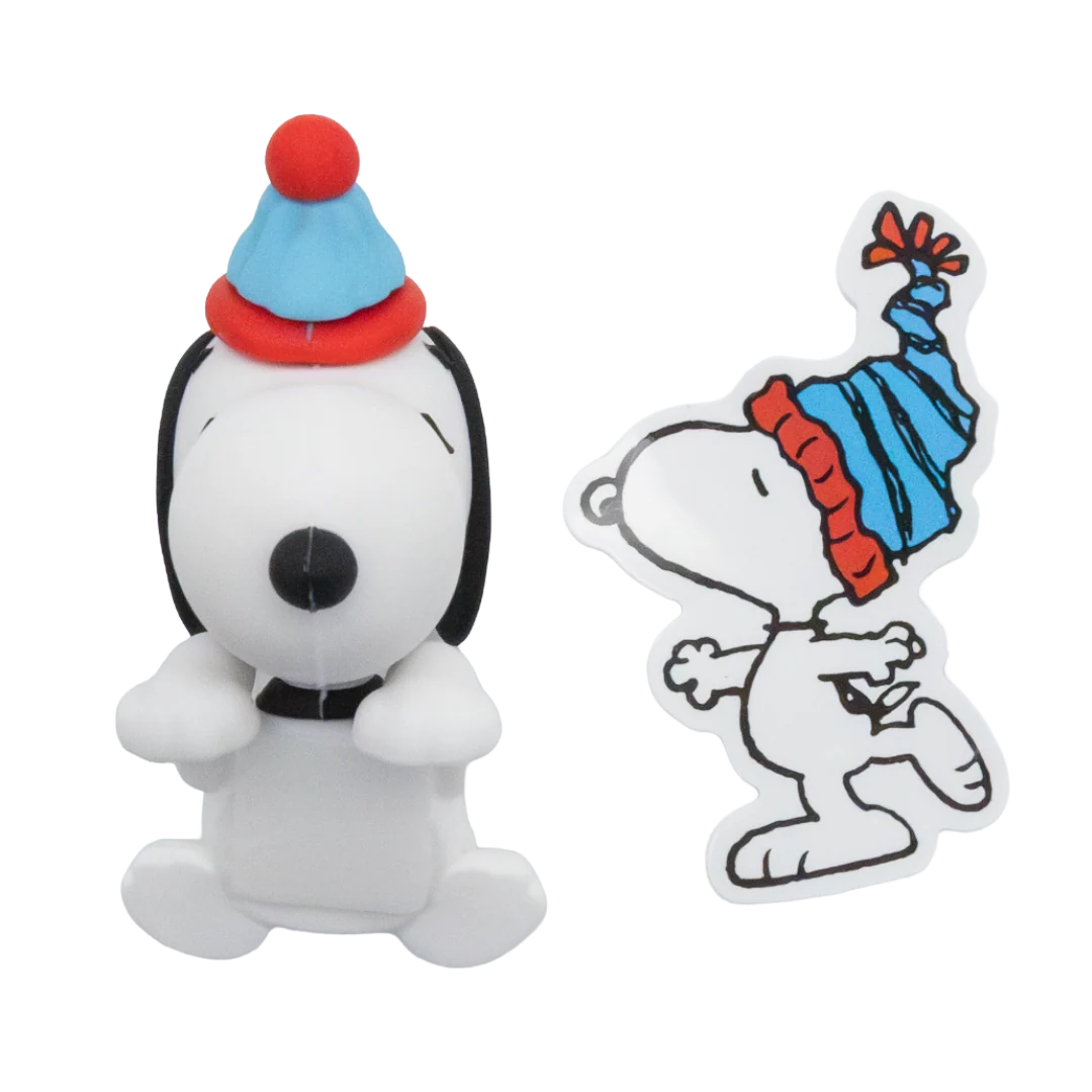 A white Snoopy character figurine wearing a blue and red striped party hat stands next to a matching die-cut sticker of Snoopy in the same hat on a plain white background.