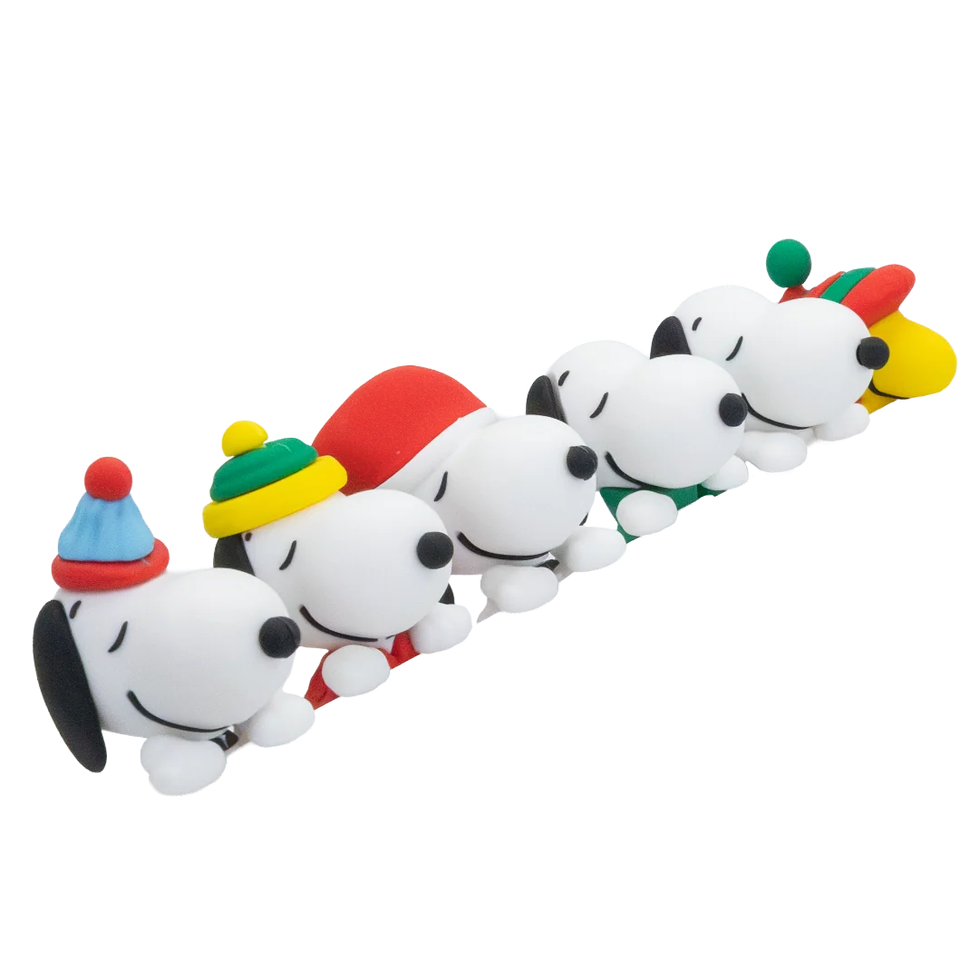 A row of Snoopy plush dog toys lined up diagonally, each wearing a different colorful holiday hat on a plain white background.