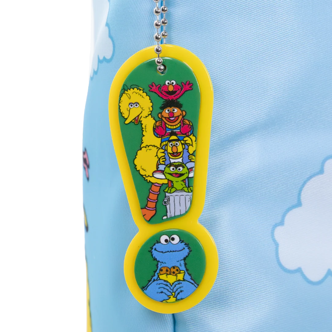 A Sesame Street keychain featuring characters Big Bird, Bertie, Ernie, Cookie Monster, and the Great Golden Feeder on a yellow and green exclamation mark design, attached to a silver ball chain and shown against a light blue patterned fabric background.