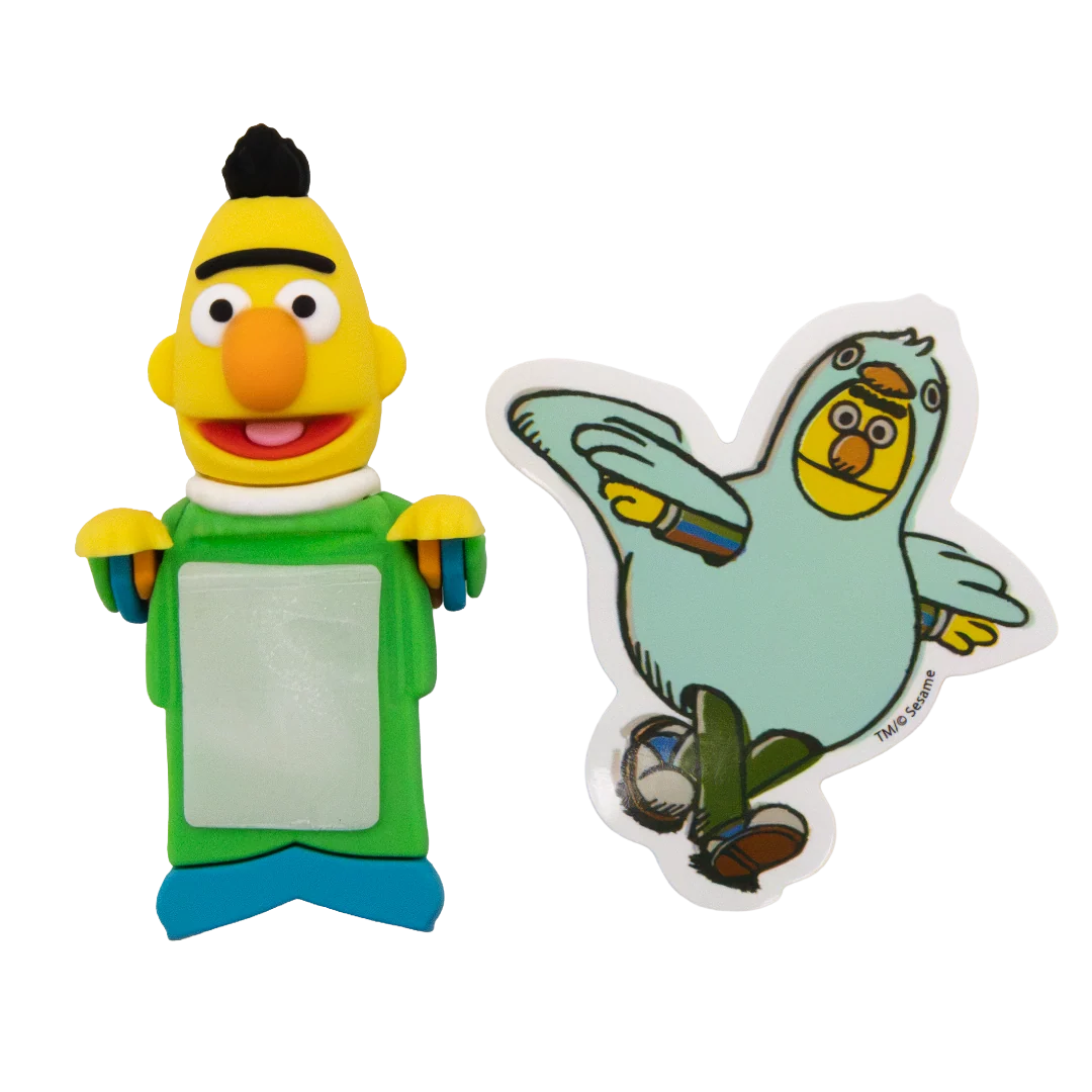 Two small character-themed items on a plain white background: a yellow puppet-like figure with a green torso and blue feet holding a blank white panel, and a die-cut sticker or decal of a light blue bird character with a yellow face.