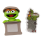 Sesame Street Oscar the Grouch collectible figure shown next to its custom nameplate sticker. The figure features green skin, brown eyes, an orange mustache, and a khaki-colored hat, standing behind a gray nameplate base.