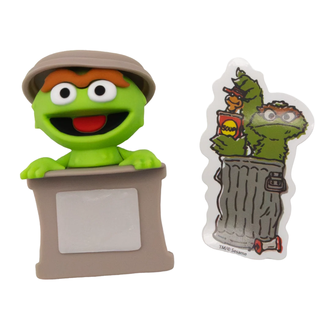 Sesame Street Oscar the Grouch collectible figure shown next to its custom nameplate sticker. The figure features green skin, brown eyes, an orange mustache, and a khaki-colored hat, standing behind a gray nameplate base.