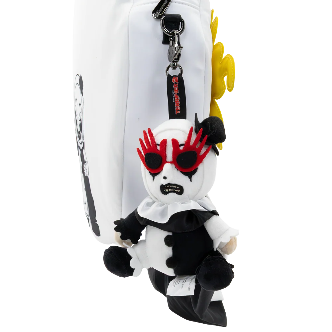 A plush character keychain or bag charm hanging from a white zipper pouch. The character has a white face and body with black clothing, red spiky sunglasses, and a yellow flower-like hair accent, shown against a plain white background.