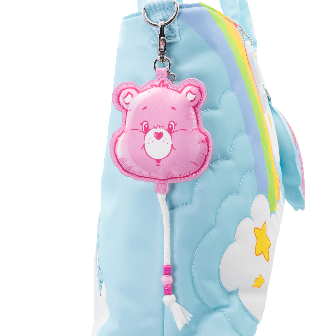 Pink bear keychain attached to a blue plush bag with rainbow and cloud design.