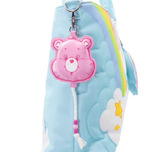 Pink bear keychain attached to a blue plush bag with rainbow and cloud design.