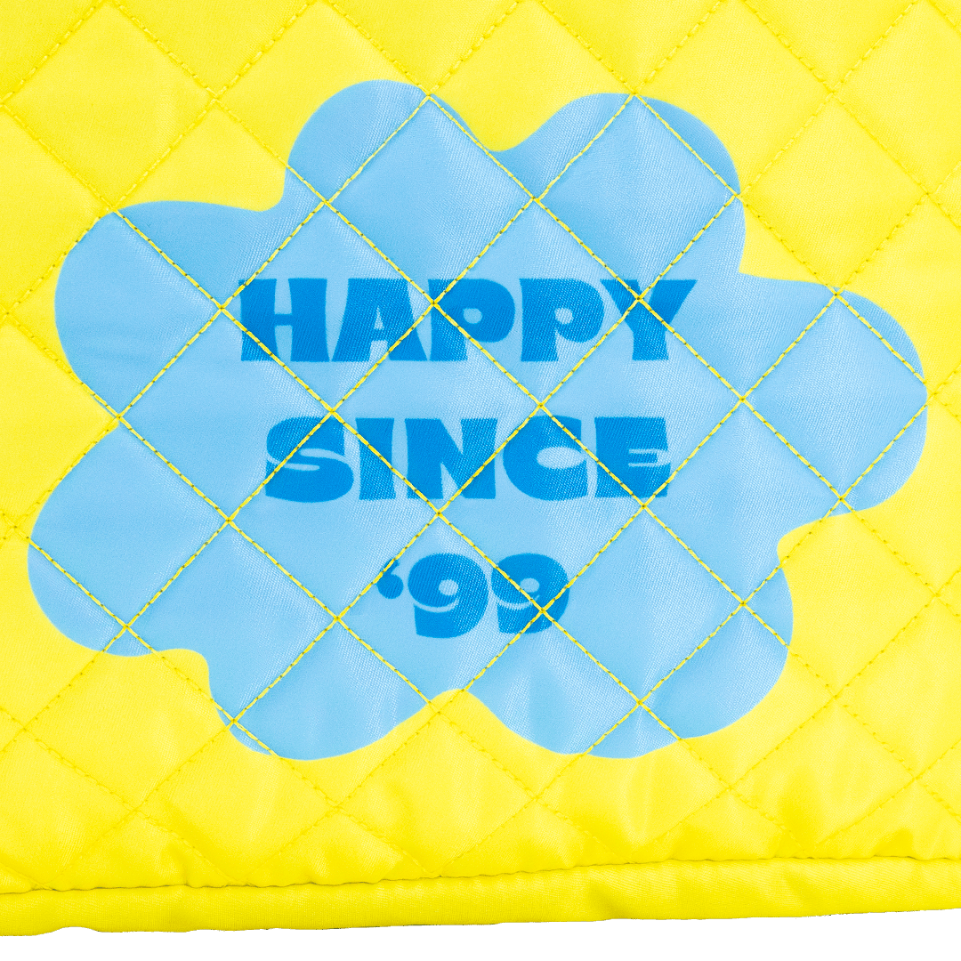 Yellow quilted pillow with blue flower-shaped patch displaying 'Happy Since '99'.