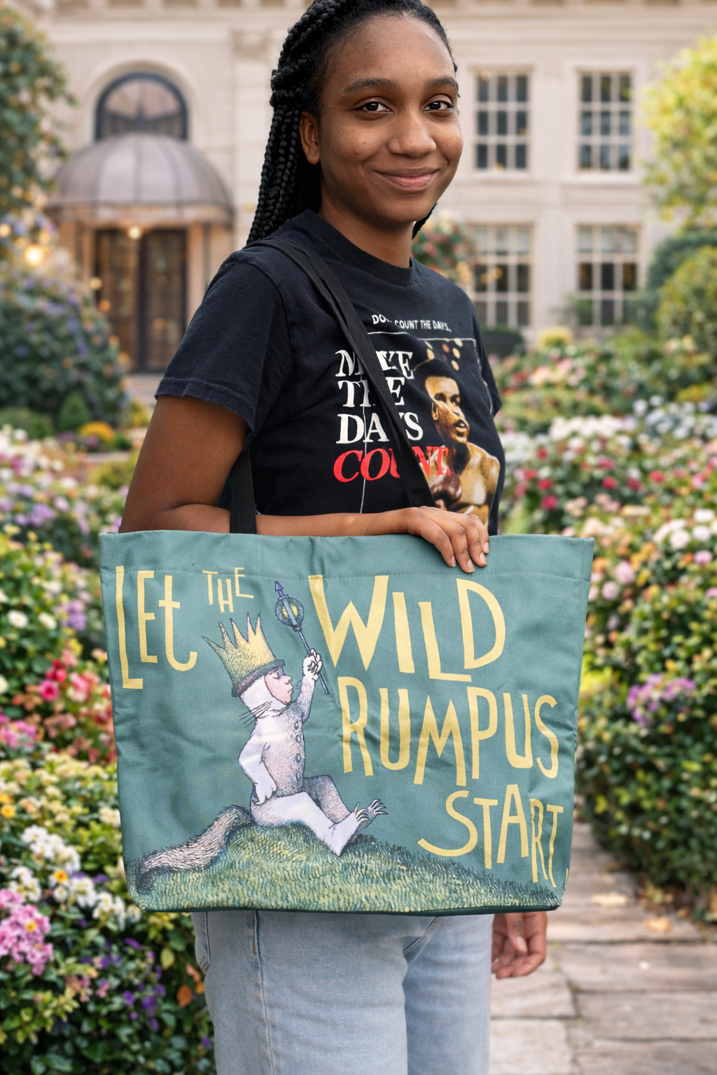 Person holding a tote bag with a design and text, standing in a garden.