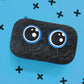 Black textured pouch with blue circular designs on a blue background with black cross symbols.