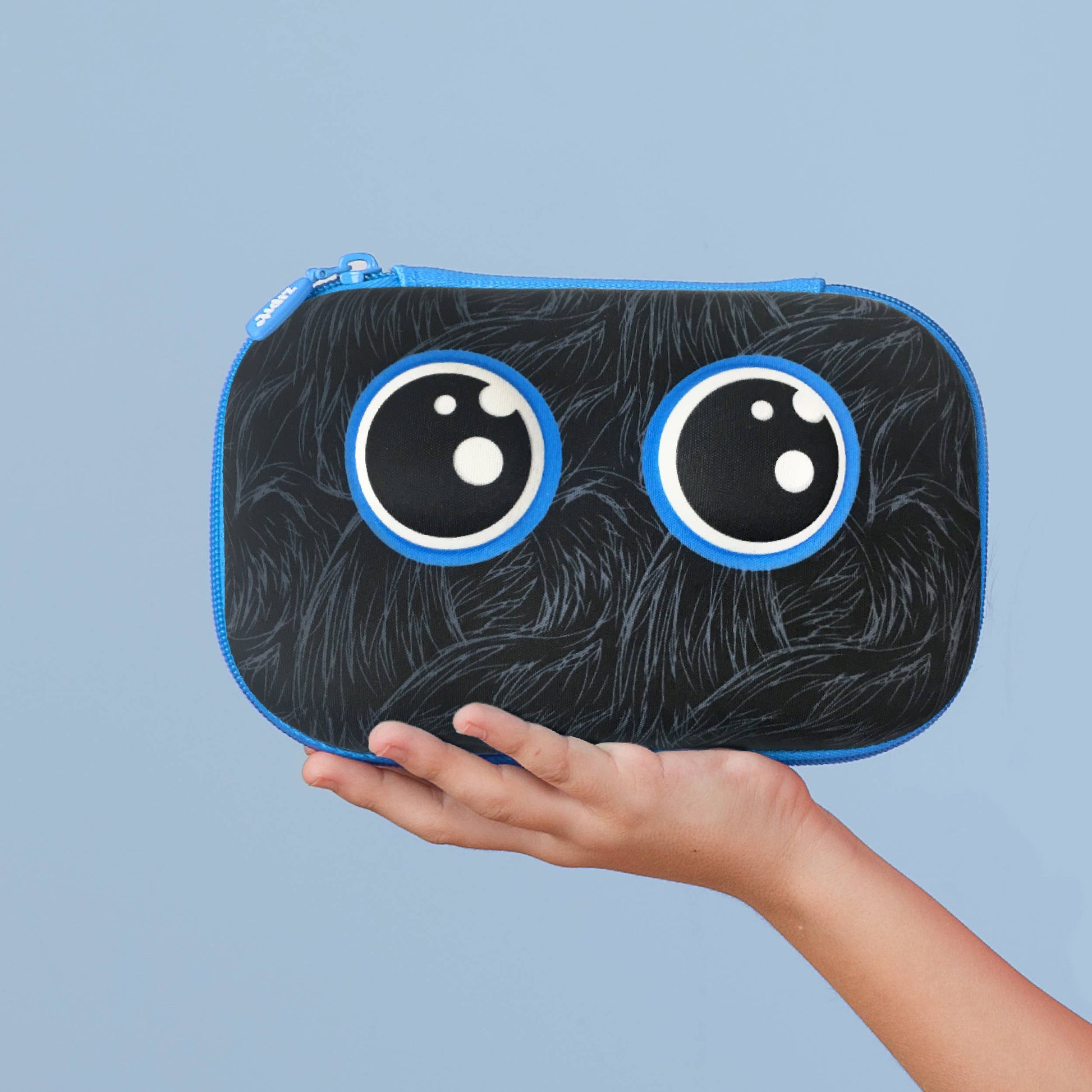 Black pouch with cartoonish eyes held by a hand against a light blue background