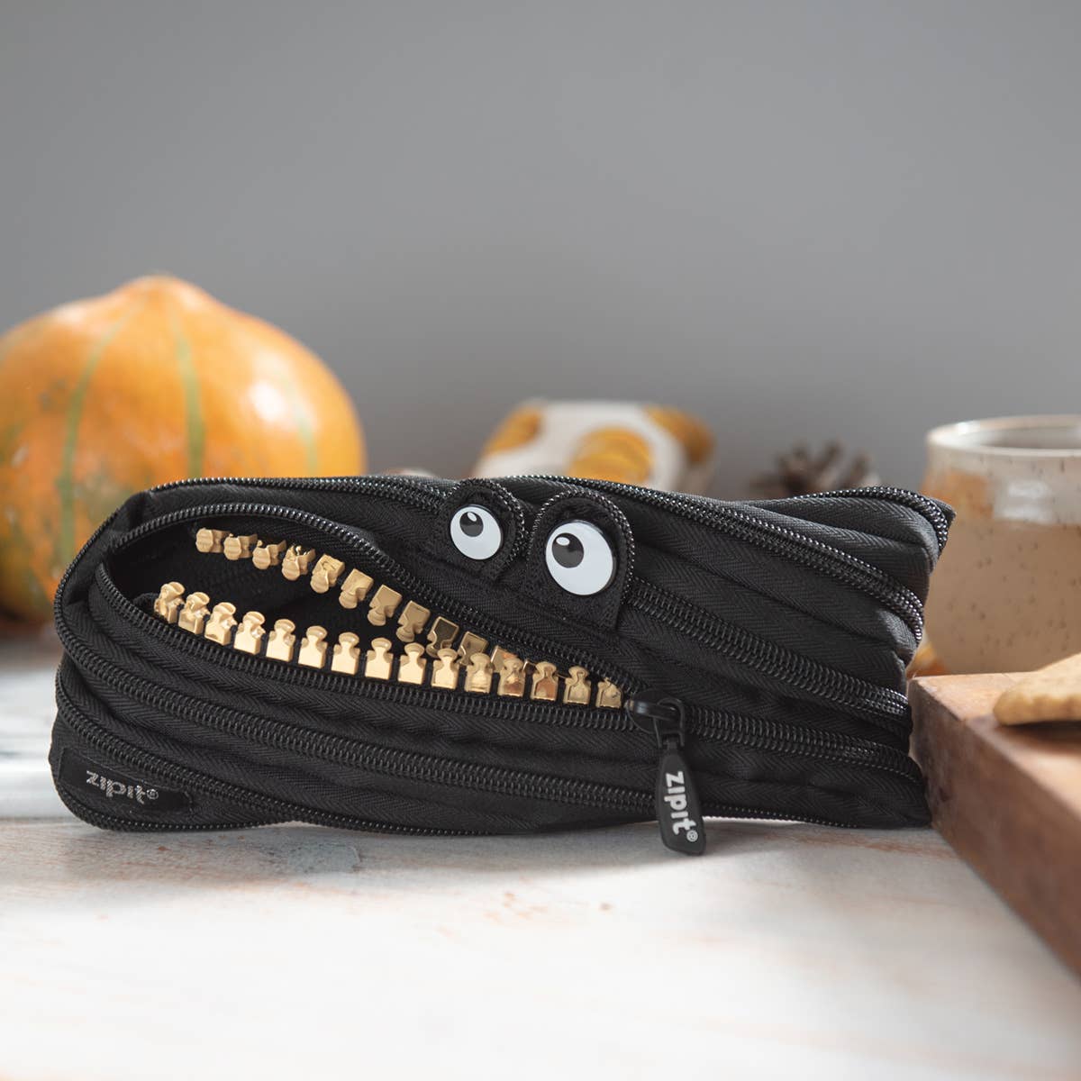 Black zipper pouch with eyes and teeth design on a surface with pumpkins in the background