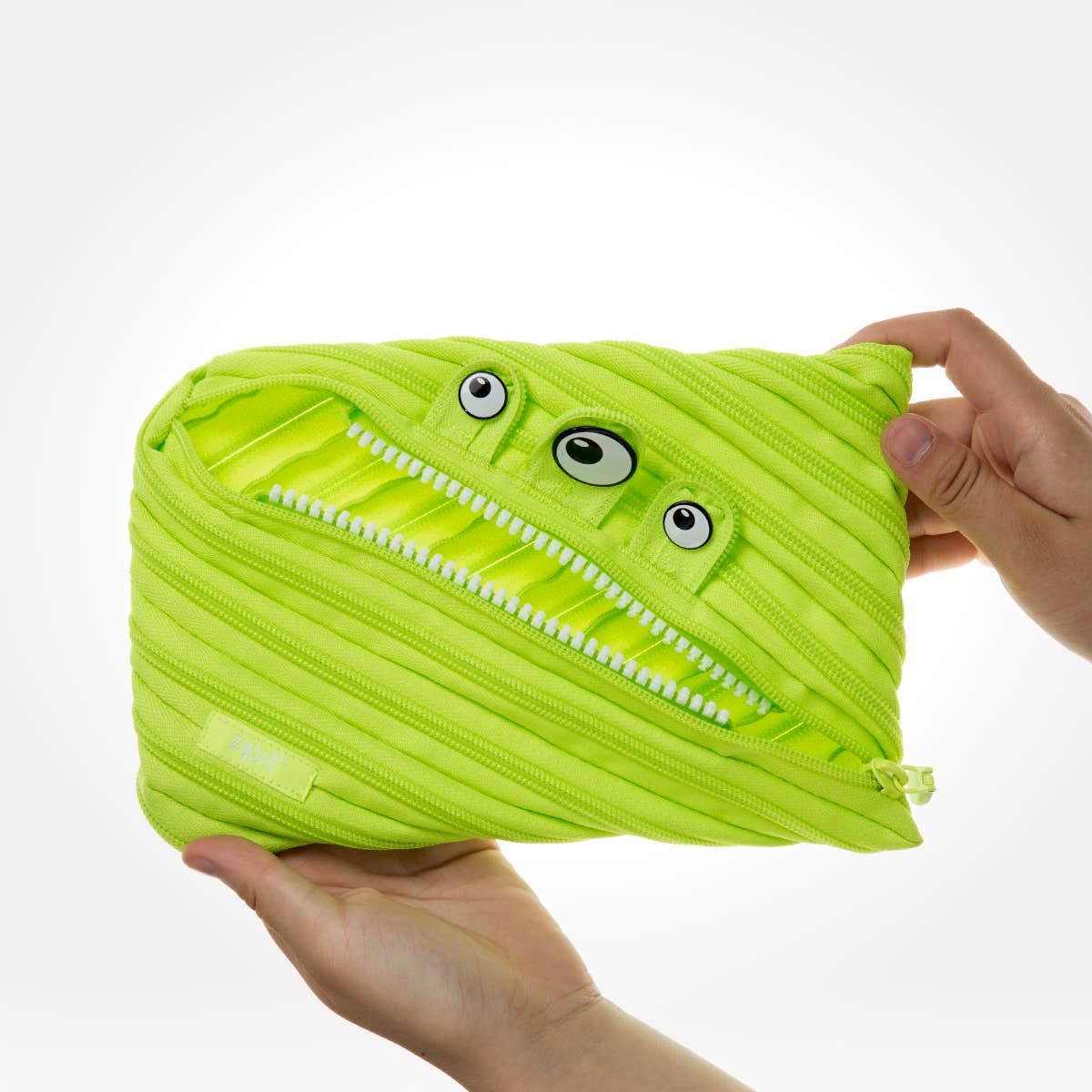 Green monster-shaped pouch with a zipper held by a hand on a white background