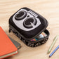 Black pencil case with white logo on a wooden surface with stationery items.