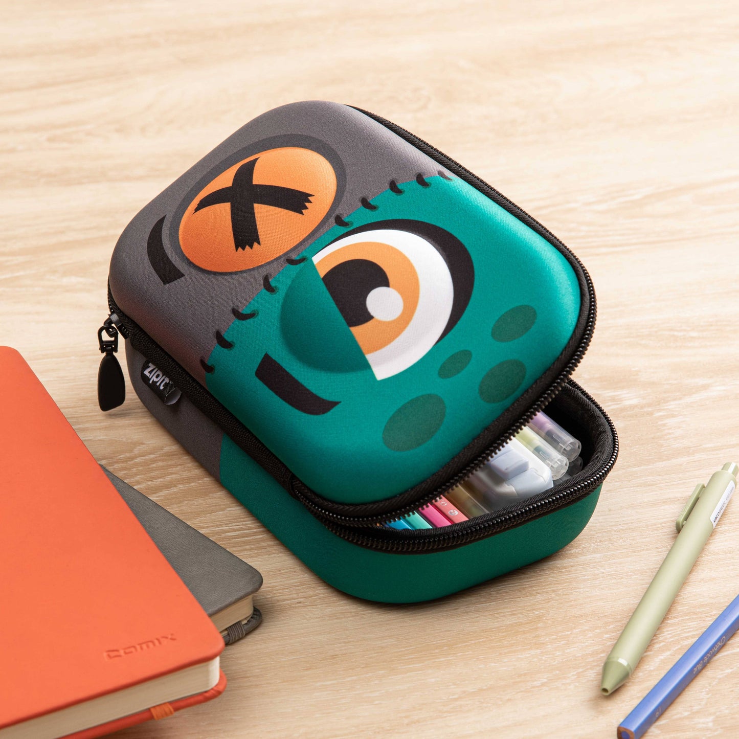 Green and black pencil case with cartoon face design on a wooden surface