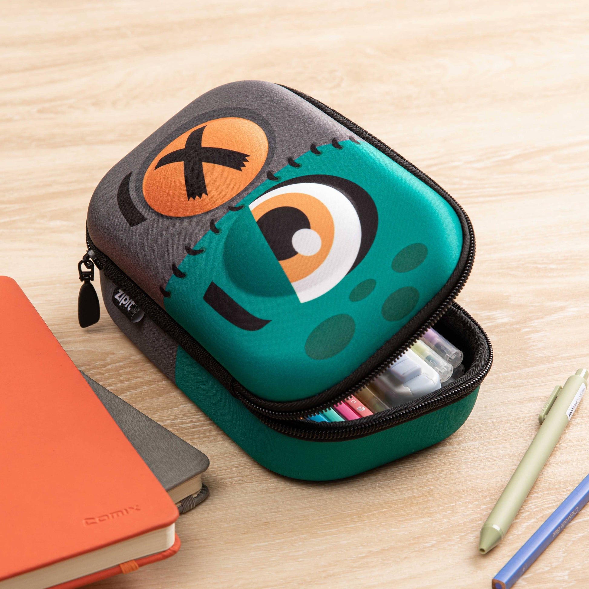 Green and black pencil case with cartoon face design on a wooden surface